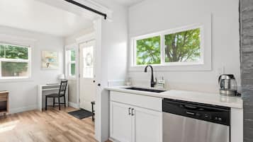 A modern kitchen with a dishwasher, a coffee maker, and a window with a view of trees.