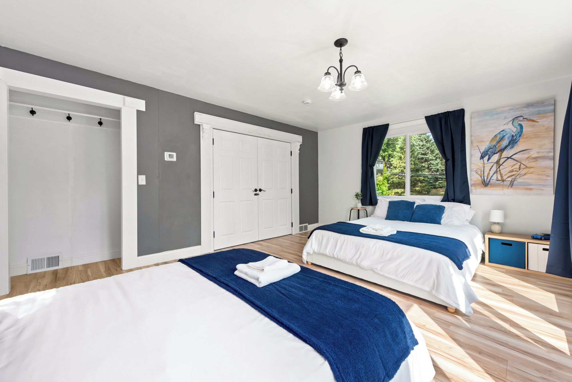 A hotel room with two beds, a large window with curtains, a painting on the wall, and a ceiling light fixture.