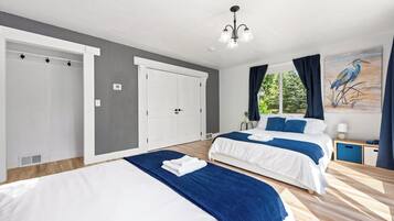 A hotel room with two beds, a large window with curtains, a painting on the wall, and a ceiling light fixture.