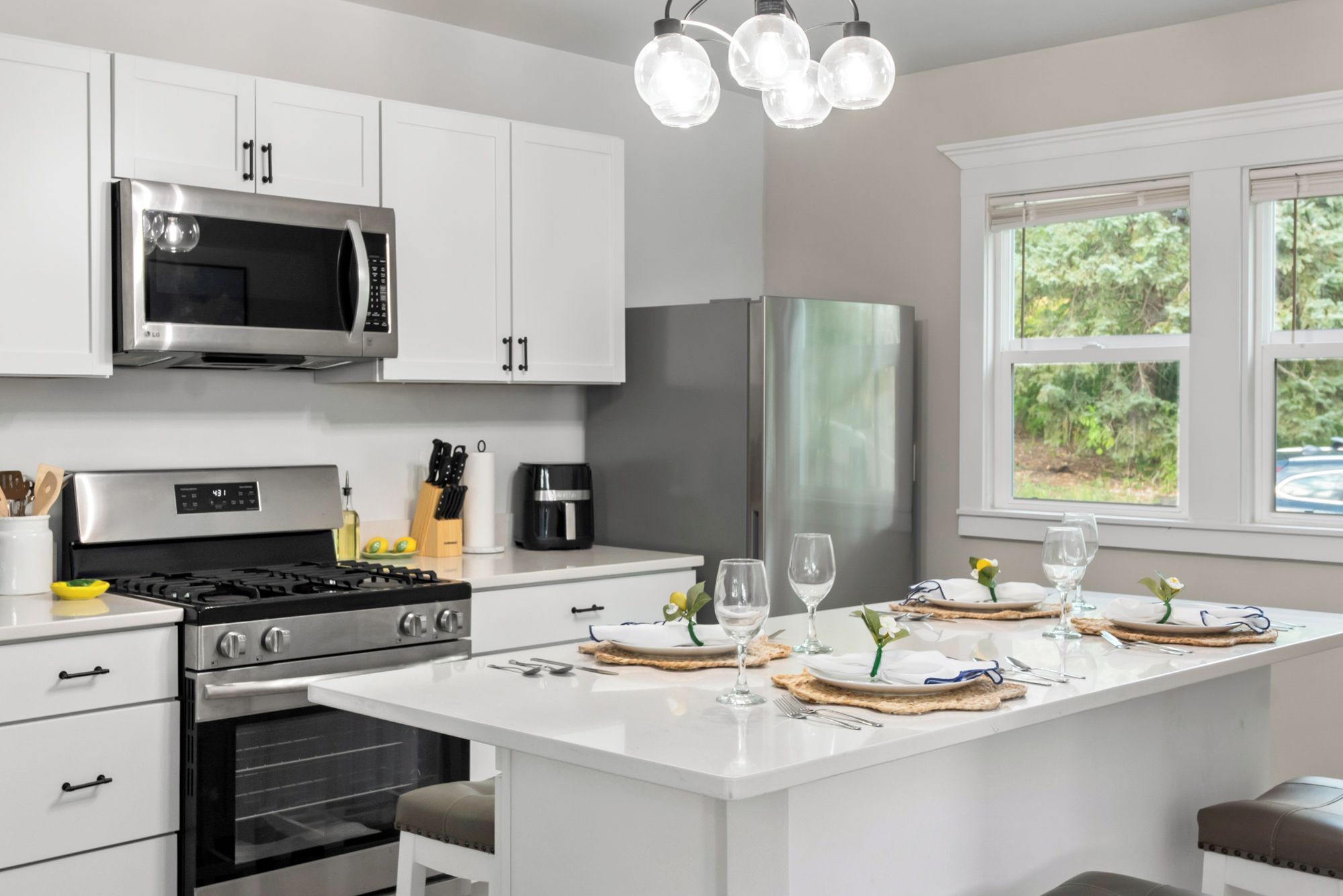 A modern kitchen with white cabinetry, stainless steel appliances, and a breakfast bar with a view of greenery outside.