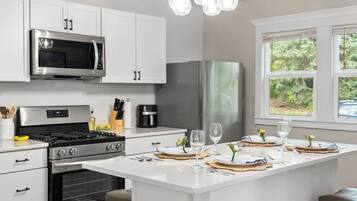 A modern kitchen with white cabinetry, stainless steel appliances, and a breakfast bar with a view of greenery outside.