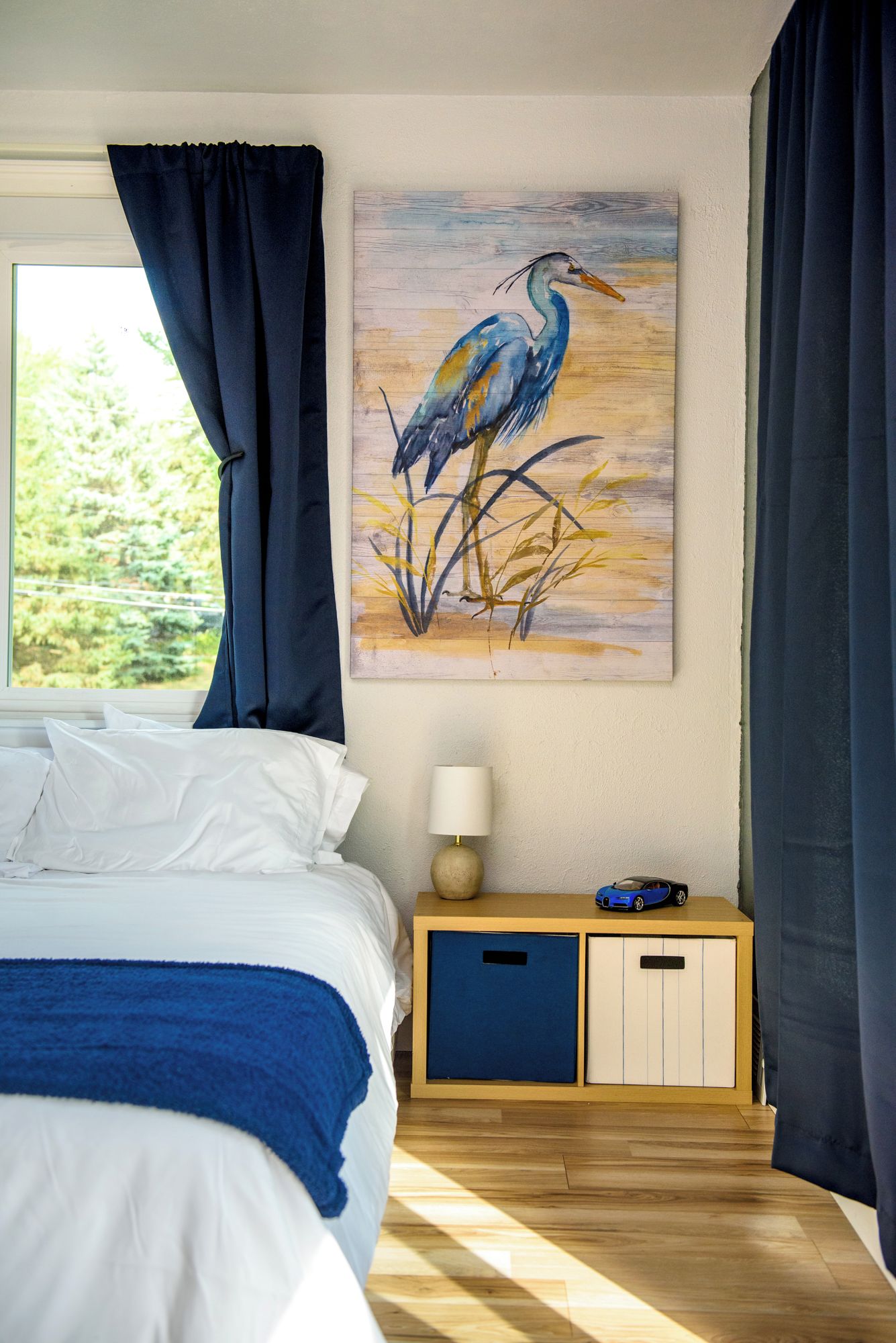 A bedroom with a bed, a nightstand, a lamp, a cabinet, and a painting of a bird on the wall.