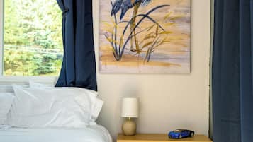 A bedroom with a bed, a nightstand, a lamp, a cabinet, and a painting of a bird on the wall.