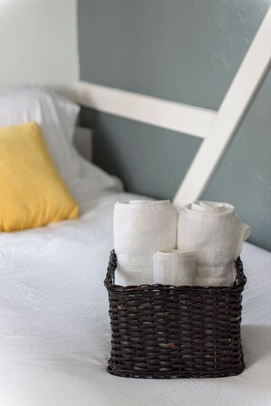 Ein Bett mit weißer Bettdecke, einem gelben Kopfkissen und einem Korbwäscheschrank mit zusammengerollten Handtüchern.
