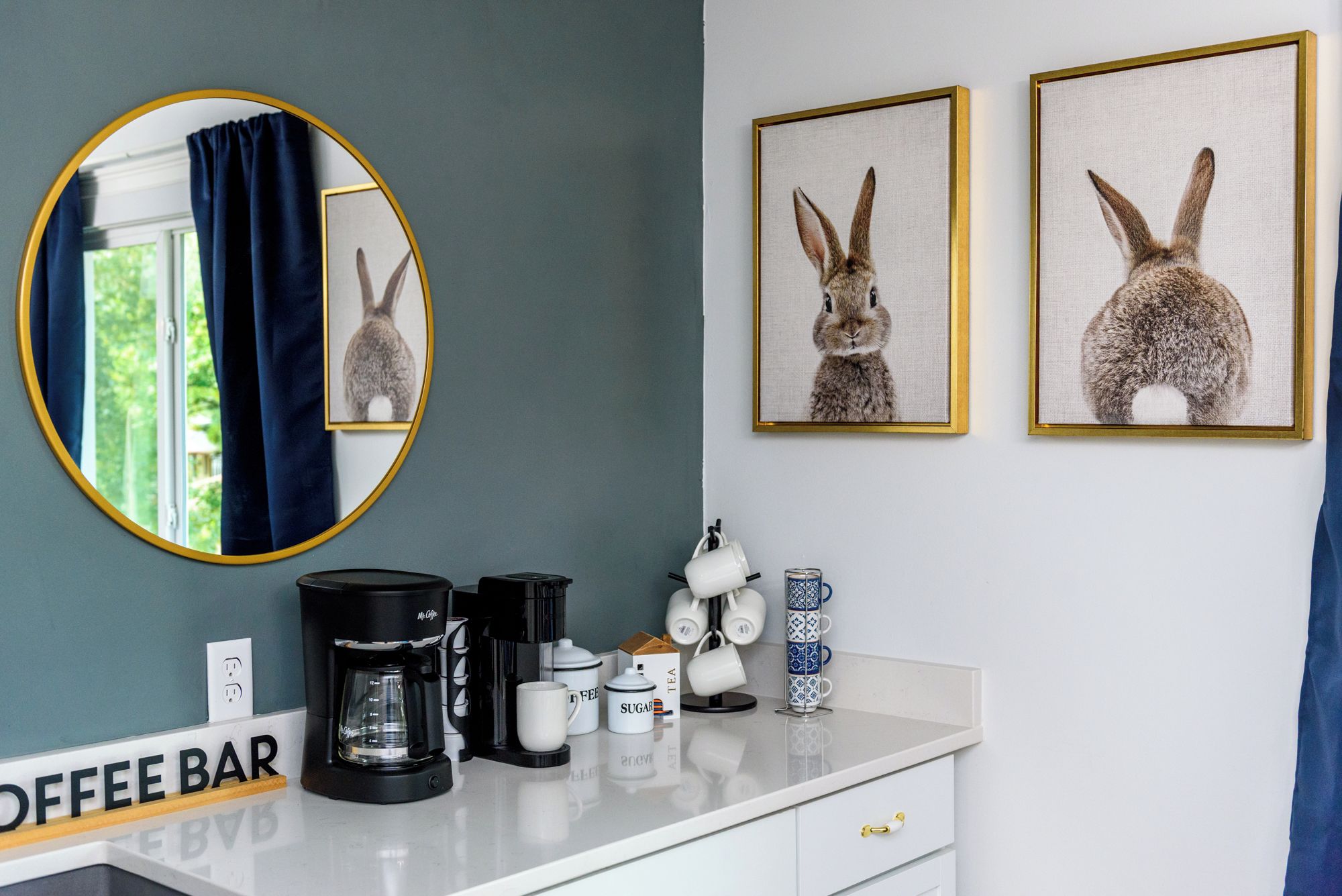 A room with a coffee bar, a mirror, and two framed rabbit pictures on the wall.