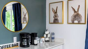A room with a coffee bar, a mirror, and two framed rabbit pictures on the wall.