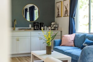 A modern living room with a blue sofa, a coffee bar in the background, and a round mirror above it.