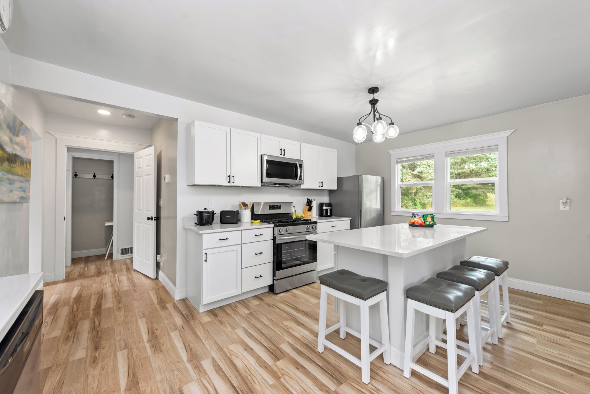 A modern kitchen with white cabinetry, a central island with stools, a microwave, oven, and a refrigerator.