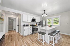 Una cocina moderna con armarios blancos, una isla central con taburetes, un microondas, horno y refrigerador.
