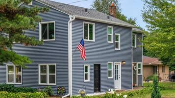 A two-story house with a front porch, a flag, and a well-maintained garden.