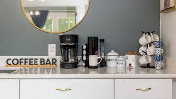 A coffee bar setup with a coffee maker, cups, sugar, and tea.