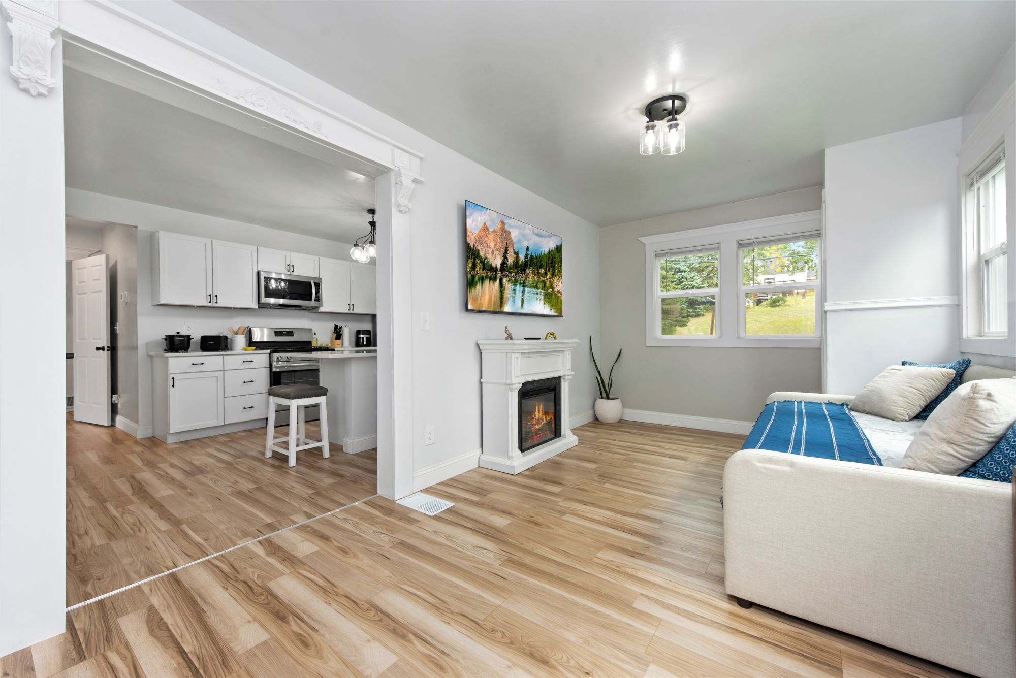 A modern living room with a fireplace, a sofa, and a kitchen area with white cabinetry and a microwave.