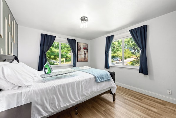 A bedroom with a bed, a window, a painting, and a ceiling light.