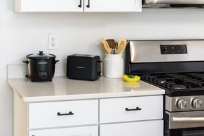 A kitchen with a stove, a toaster, a slow cooker, and a spice rack.