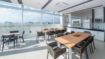 Un espacio de oficina moderno con una mesa grande y sillas, una zona de cocina y amplias ventanas con vistas a la ciudad.