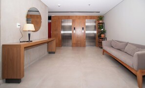 A modern lobby with a reception desk, a sofa, a mirror, and two elevators. - Sunny Retreat with Pool, Gym and City Views (Asunción)