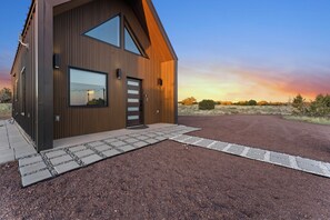 A modern two-story building with a sloped roof, large windows, and a gravel driveway leading to a wooden door. - AEA - Woodland AZ (Valle)