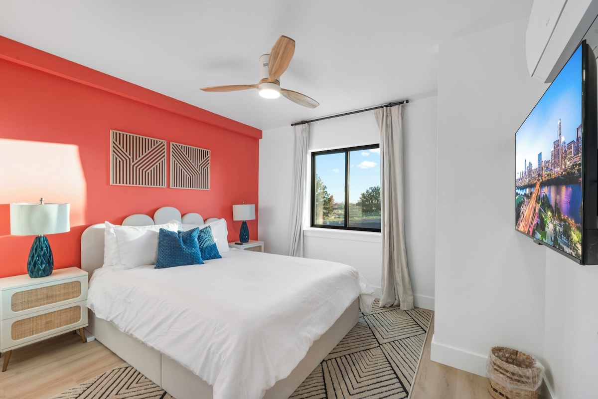 Een hotelkamer met een bed, een plafondventilator, een raam met gordijnen, een tv aan de muur en een decoratief wandpaneel.
