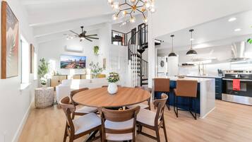 A modern kitchen with a central island, a dining area with a round table, and a staircase leading to an upper level.