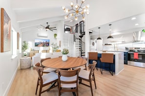 Een moderne keuken met een centraal eiland, een eethoek met een ronde tafel, en een trap die naar een hoger gelegen verdieping leidt.
