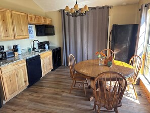 Een keuken met houten kastjes, een eettafel met stoelen, een kroonluchter en een koelkast.