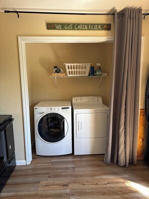 Een wasserette met een wasmachine, droger en een plank met wasmiddelen.