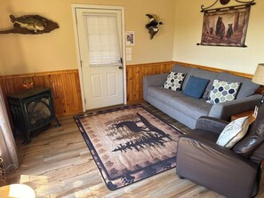 Een woonkamer met een houten vloer, een grijze bank met decoratieve kussens, een tapijt met een ontwerp van een hert en een boom, en een vis aan de muur.