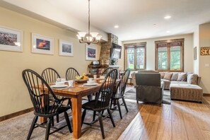 Gather around the handsome wood dining table for meals and laughter, then unwind on the plush sectional by the stone fireplace. Natural light pours through the windows, warming the space and inviting you to relax. - Golf Course Views | Private Hot Tub (Mammoth Lakes)