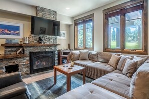 Sink into plush seating by your stone fireplace, where large windows frame tranquil views of the surrounding green. The perfect spot to unwind after your adventures. - Golf Course Views | Private Hot Tub (Mammoth Lakes)