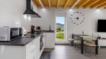 Een moderne keuken met een magnetron, broodrooster en koffiezetapparaat, een eethoek met tafel en stoelen, en een groot raam met uitzicht op een groen landschap.