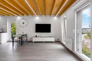 Un espacio habitable moderno con comedor, un televisor de pantalla plana en la pared y vistas a través de amplias ventanas.