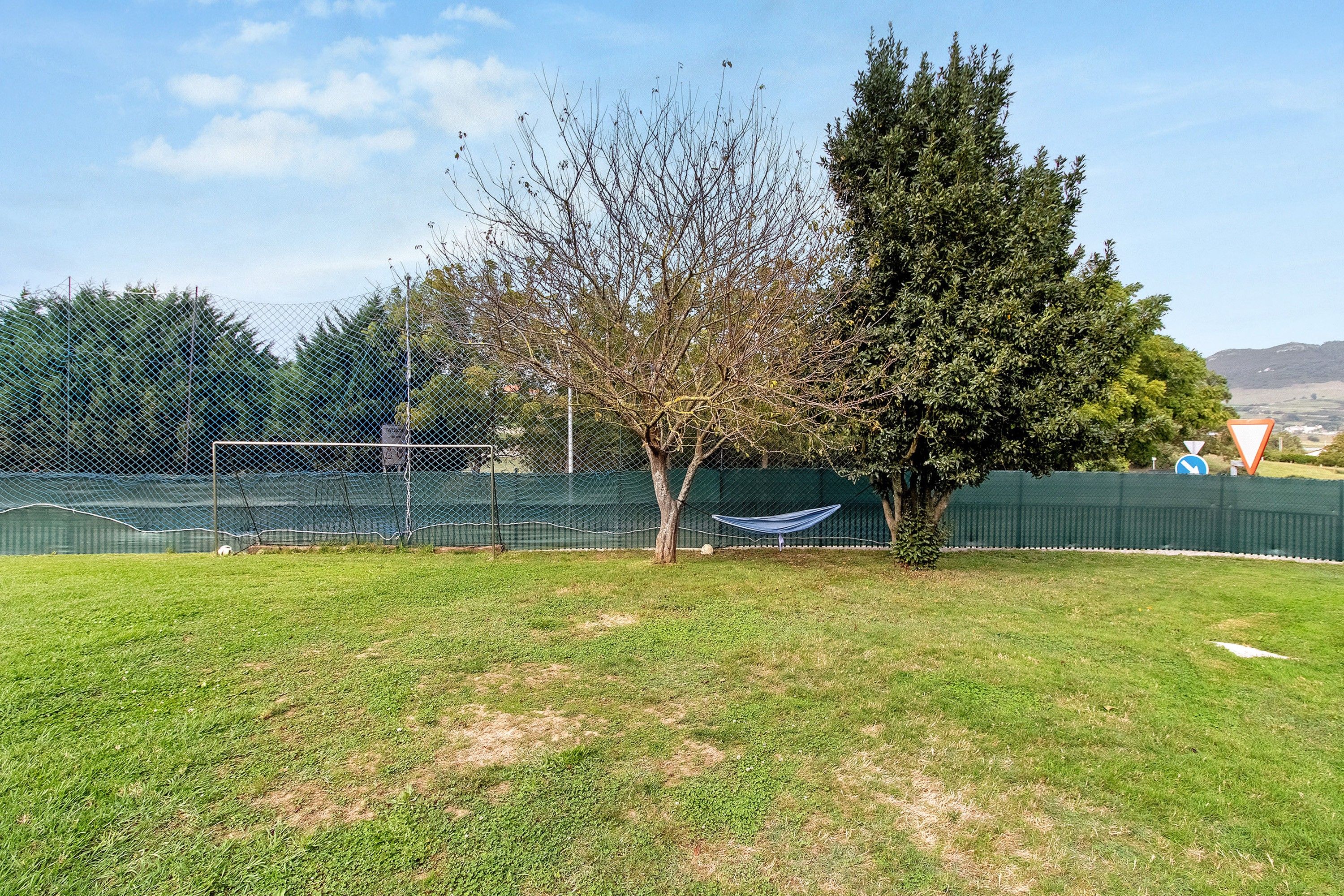 A fenced outdoor area with grass, trees, and a hammock.