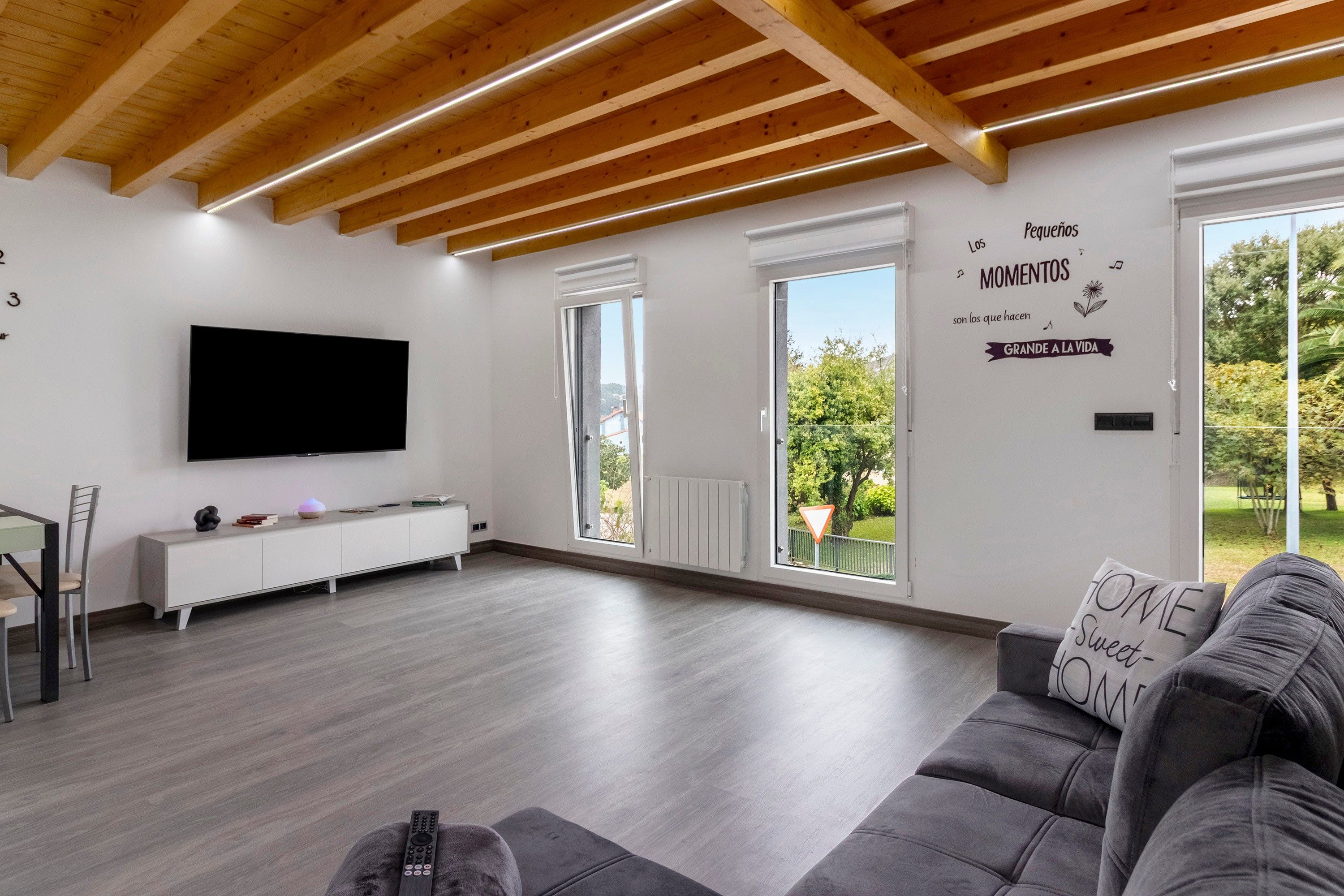 A modern living room with a flat-screen TV, a sofa, and a dining area with a chair and table.