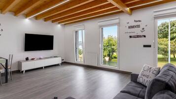A modern living room with a flat-screen TV, a sofa, and a dining area with a chair and table.