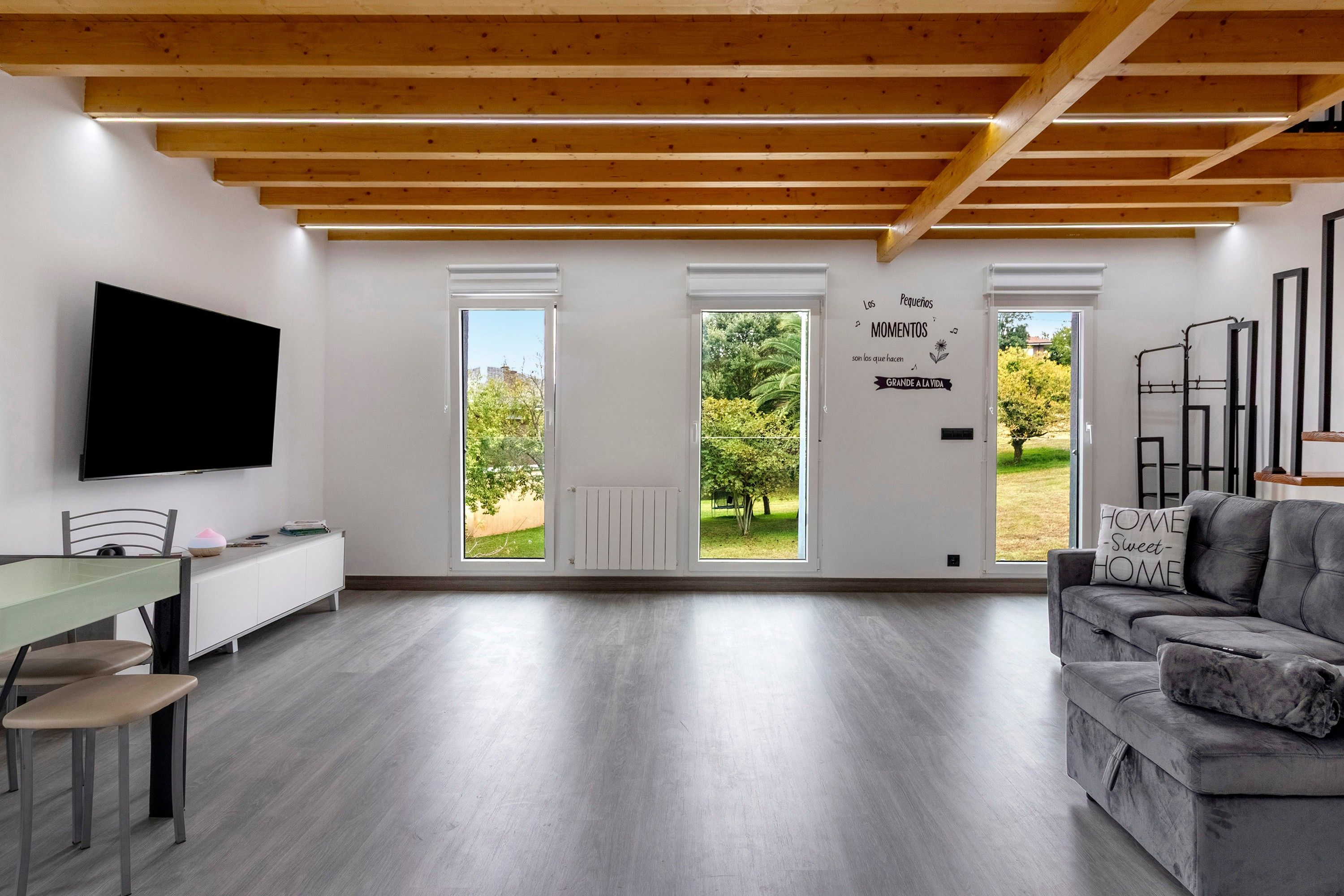 Una sala de estar moderna con un televisor de pantalla plana, un sofá gris y un comedor con mesa y sillas.