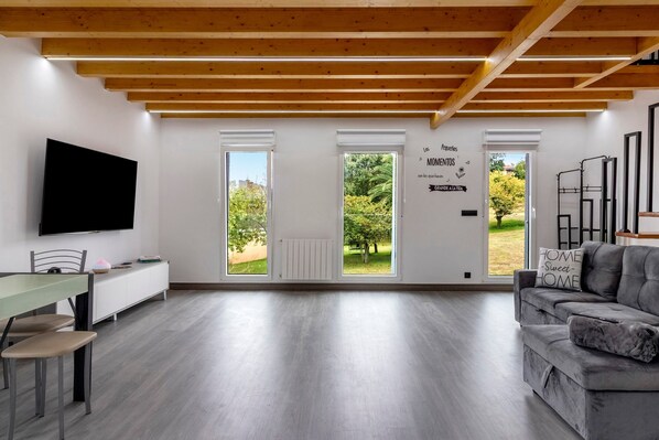 Una sala de estar moderna con un televisor de pantalla plana, un sofá gris y un comedor con mesa y sillas.