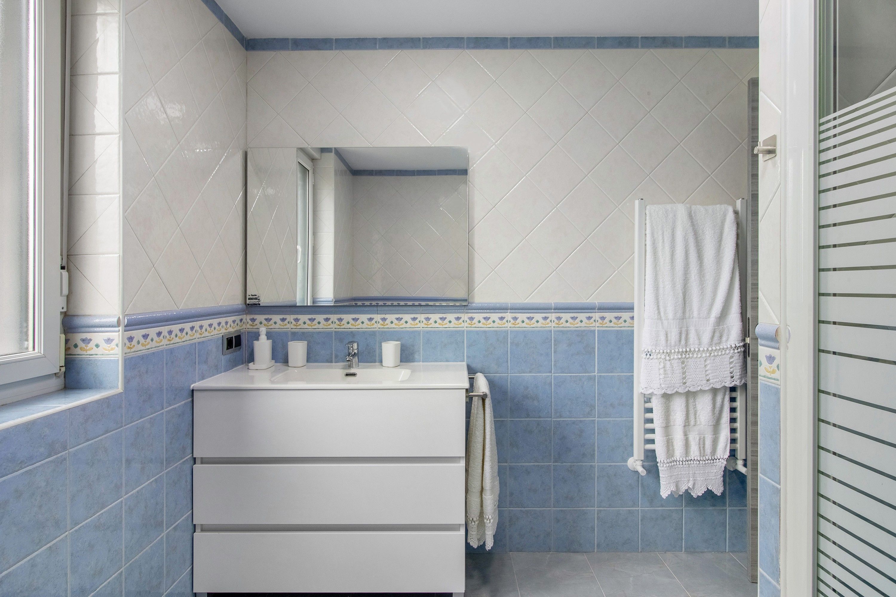 A bathroom with a white sink, a mirror, and a towel hanging on a rack.