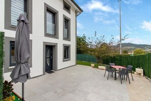 A modern two-story building with a patio area featuring outdoor seating and a covered umbrella.