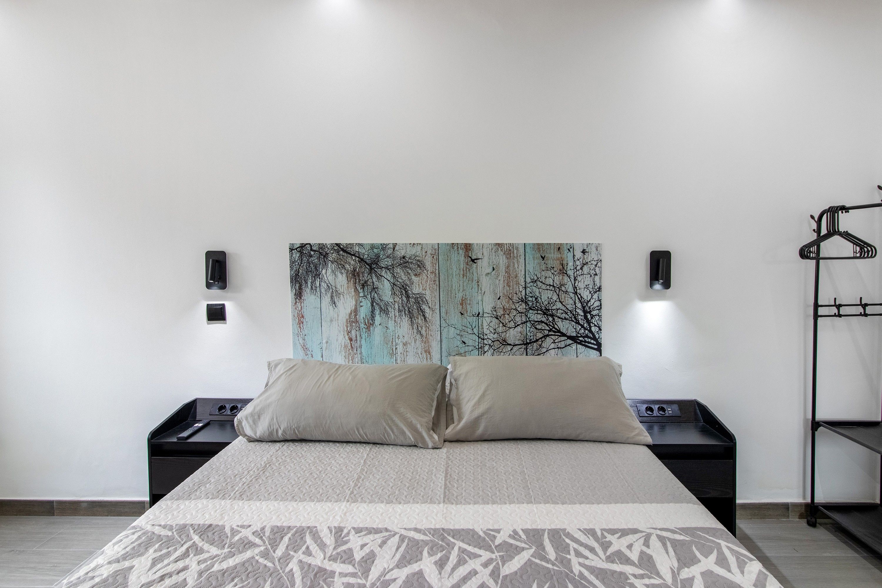 Ein Schlafzimmer mit einem Bett, zwei Nachttischen, einer Wandleuchte und einem Kleiderhaken.
