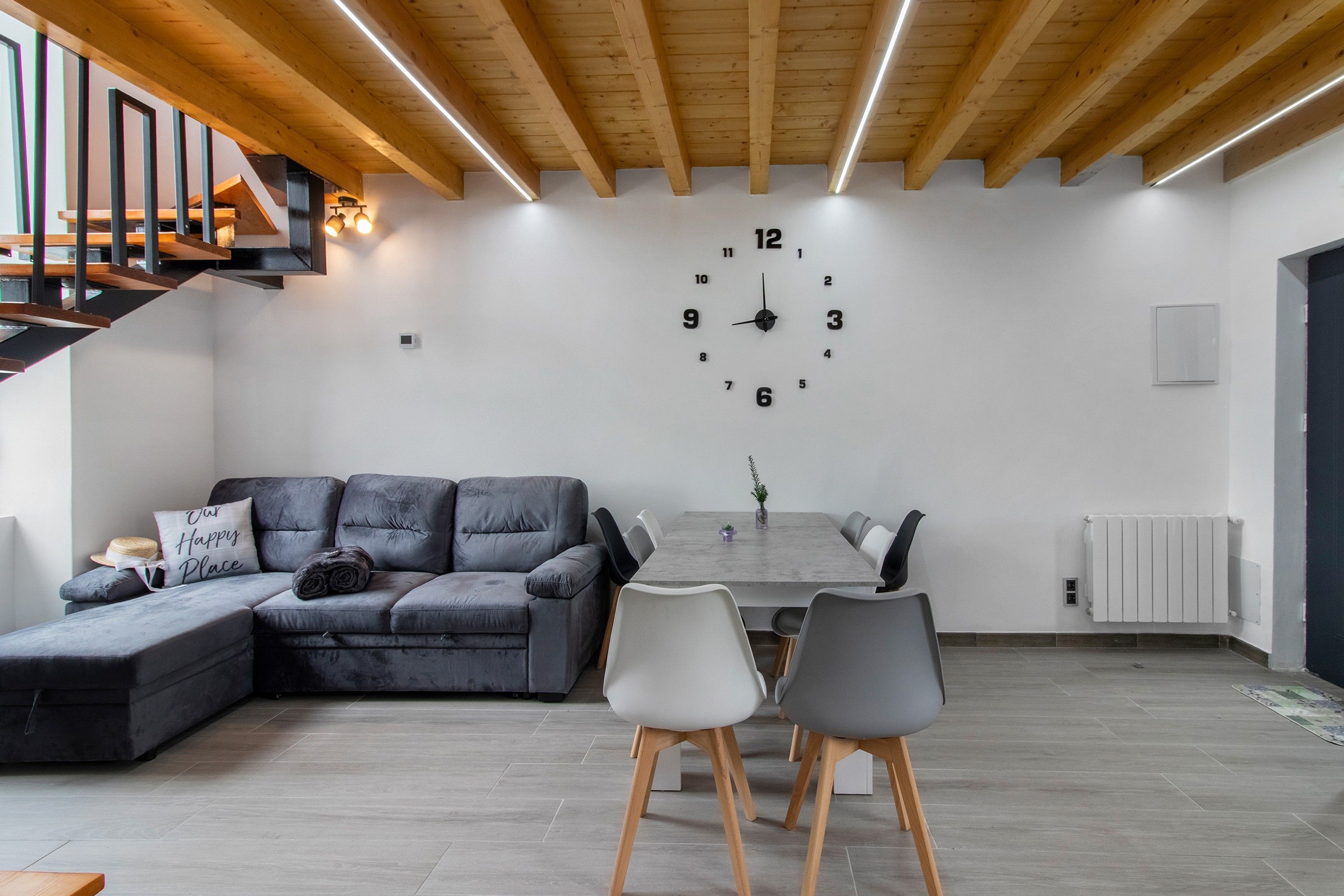 Een moderne woonkamer met een hoekbank, een eettafel met stoelen en een grote wandklok.