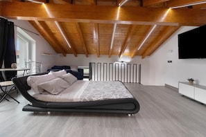 A modern bedroom with a large bed, a desk, and a TV.