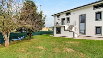 Una casa moderna de dos pisos con balcón, patio cercado y hamaca.
