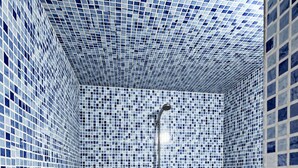 Ein Badezimmer mit Schachbrettfußboden, einer Dusche mit Handbrause und Wänden, die mit blau-weißen Mosaikfliesen verziert sind.