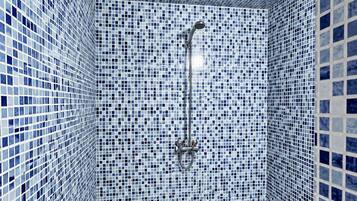 A bathroom with a checkered floor, a shower with a handheld showerhead, and walls covered with blue and white mosaic tiles.
