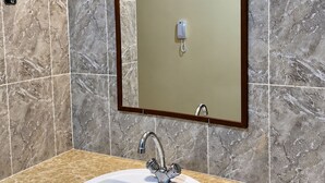 Ein Badezimmer mit einer Marmorfliesenwand, einem weißen Waschbecken mit einem einzelnen Wasserhahn und einem Spiegel mit einer Leuchte darüber.