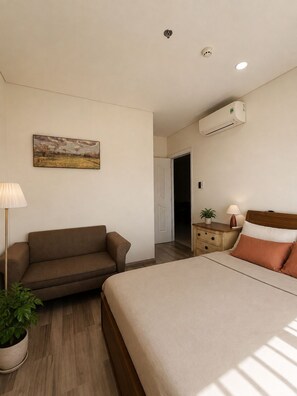 A bedroom with a bed, a nightstand, a lamp, a potted plant, and a painting on the wall. - Calm 2BR Apt | Big Balcony, Pool & Central (Đà Nẵng)
