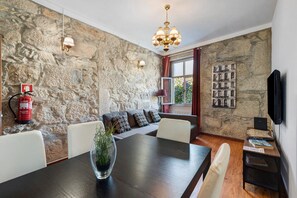 A dining area with a stone wall, a fire extinguisher, a chandelier, and a television on the wall. - Apartment 'Fontainhas Stone' with Wi-Fi (Porto)