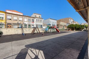 A playground with swings and slides, adjacent to a building with a red roof. - Apartment 'Balcony Porto's' with Balcony, Wi-Fi and Air Conditioning (Porto)