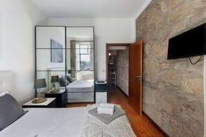 A hotel room with a bed, bedside tables, a mirror, a television, and a stone wall. - Apartment 'Balcony Porto's' with Balcony, Wi-Fi and Air Conditioning (Porto)