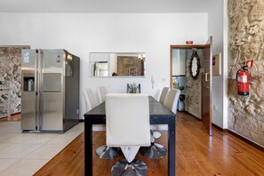A dining area with a table, chairs, a refrigerator, a fire extinguisher, and a stone wall. - Apartment 'Balcony Porto's' with Balcony, Wi-Fi and Air Conditioning (Porto)